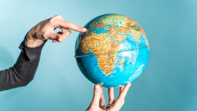 une main et un doigt qui pointe un pays sur le globe